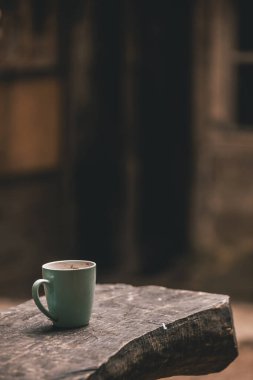 Kırsal bölgedeki ahşap masada beyaz seramik bardak. Arka planda eski kulübe bulanıklaştı