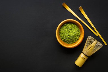 Geleneksel Japon kibrit çay seti canlı yeşil kibrit tozu ile ahşap bir kase, bambu çırpısı (chasen) ve koyu dokulu arka planda bambu kepçeleri (chashaku) ile sol tarafta kopya alanı ile birlikte.