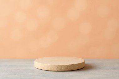 Mavi bir yüzey üzerinde yuvarlak bej bir podyumu olan basit bir sahne, yumuşak pastel şeftali arkaplanına karşı beyaz yayılmış bokeh ışığı. Ürün fotografı kurulumu