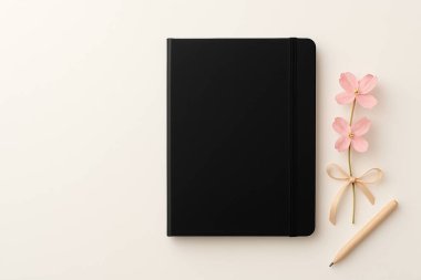 Black notebook or planner mockup with elastic band, pink flowers, and a wooden pen on a light beige background. Ideal for organization, business, diary, or design projects.
