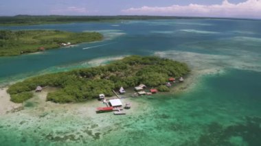 Panama 'daki Bocas del Toro Adası' nın turkuaz lagün manzaralı ve deniz aşırı orman evlerinin insansız hava aracı dairesel videosu. 