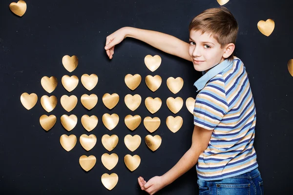 Uśmiechnięty chłopiec trzyma złote serce na ciemne tło teksturowane — Zdjęcie stockowe