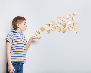 Altın kalpler elinden hafif gri arka plan üzerinde üfleme çocuk