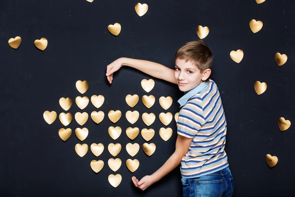 Ragazzo sorridente che tiene il cuore d'oro su sfondo scuro — Foto Stock