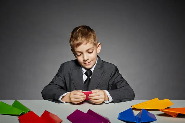 Menino em terno de negócios fazendo aviões de papel a cores — Fotografia de Stock