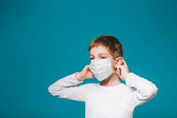 Junge setzt Schutzmaske über blauem Hintergrund auf — Stockfoto