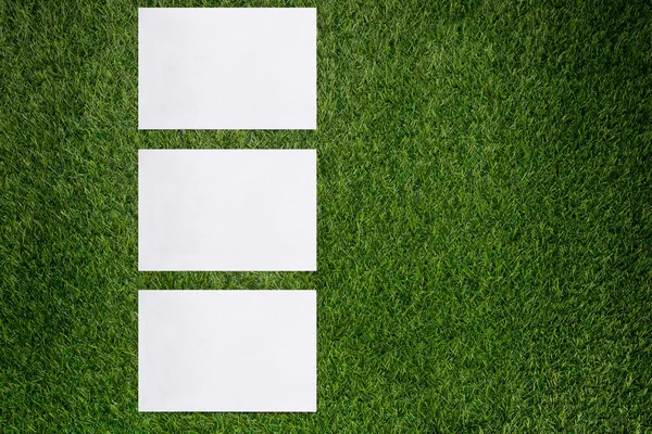 Tři bílé listy papíru ležící na zelené trávě — Stock fotografie