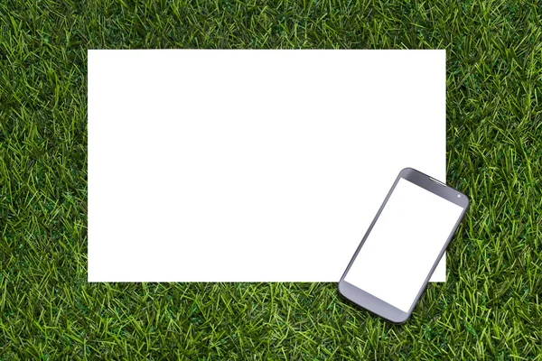 Mobilní telefon a list papíru na zelené trávě — Stock fotografie