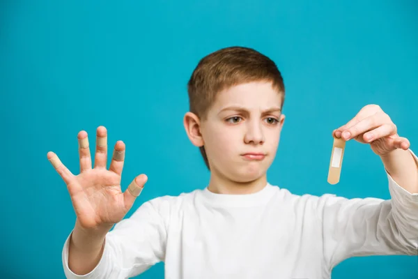 Unhappy boy in white clothes with adhesive plasters on his finge — Stock Photo, Image