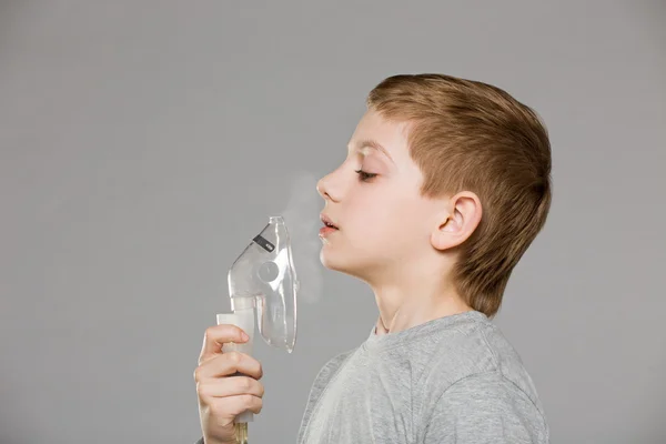 Menino respirando de máscara inalador liberando fumaça no backgr cinza — Fotografia de Stock