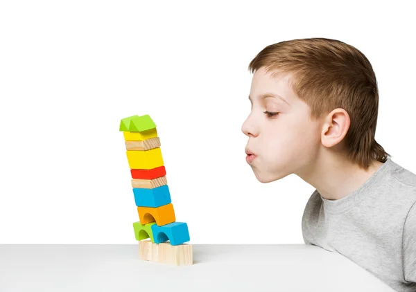 Portrait of a boy blowing on falling house made of wooden blocks — Stock Photo, Image