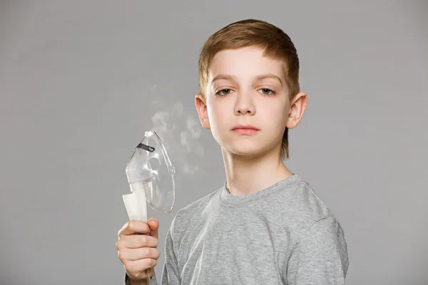 Olycklig pojke håller inhalator mask släppa rök på grå backg — Stockfoto