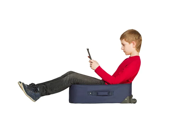 男孩坐在使用 tablet pc 上白色孤立的旅行袋 — 图库照片