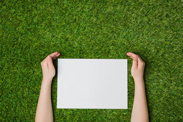 Mão segurando folha em branco de papel sobre grama verde — Fotografia de Stock