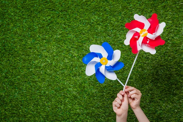 Ruce držící pinwheels trávě — Stock fotografie