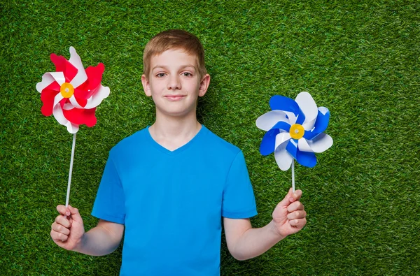 Uśmiechnięty chłopiec trzyma Wiatrowskazy nad trawa — Zdjęcie stockowe
