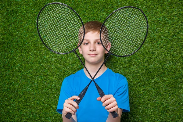 Menino feliz segurando raquetes de badminton sobre a grama — Fotografia de Stock