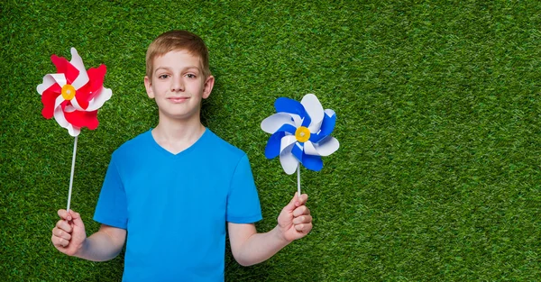 Sonriente niño sosteniendo molinillos sobre hierba —  Fotos de Stock