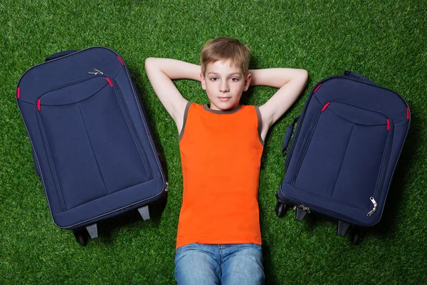 Boy with siutcases th lying on green grass — Stock Photo, Image
