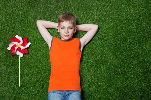 Boy lying with pinwheel  on green grass — Stock Photo, Image