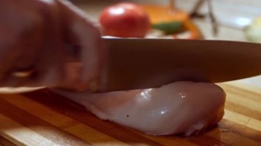 Aşçı elleri yakın plan, kadın çiğ tavuk göğsünü tahta tahtayla kesiyor..