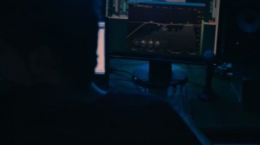 Kayıt stüdyosu. Bilgisayar monitöründe çalışan ses mühendisi sesleri düzenliyor ve dans ediyor. Düzenleme süreci. Modern teknoloji, ses ve sesin düzeltilmesi. Stüdyoda ışık zayıf
