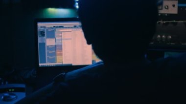 Kayıt stüdyosu. Bilgisayar monitöründe çalışan ses mühendisi sesleri düzenliyor ve dans ediyor. Düzenleme süreci. Modern teknoloji, ses ve sesin düzeltilmesi. Stüdyoda ışık zayıf
