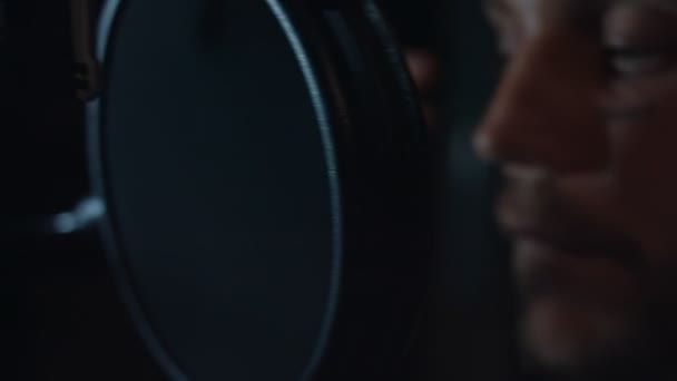 Portret van een knappe mannelijke rapzanger in een koptelefoon met professionele microfoon die een nieuw nummer opneemt in een moderne studio. Muziekproductie. Slecht licht — Stockvideo