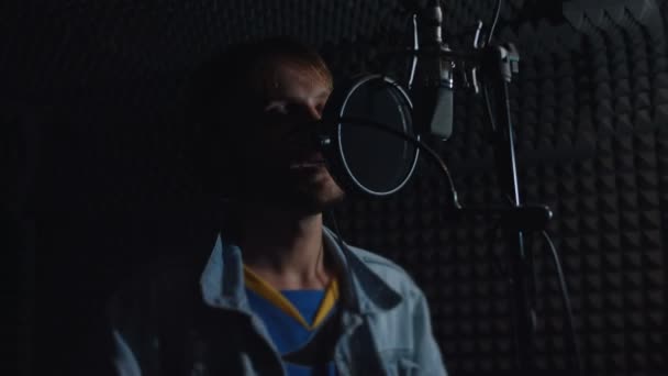 Portret van een knappe mannelijke rapzanger in een koptelefoon met professionele microfoon die een nieuw nummer opneemt in een moderne studio. Muziekproductie. Slecht licht — Stockvideo