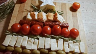 Düz peynir ve et tabağı. Noel ağacı şeklinde dizilmiş peynir, füme sosis, domates, zeytin ve rozmarin. Noel tatili için yemek. Yavaş çekim