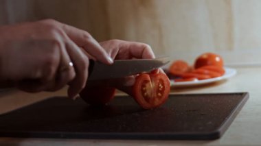 Kadın eli mutfak bıçağı kullanarak tahta üzerinde taze domates dilimliyor. Sağlıklı beslenme. Kesilmiş domates..