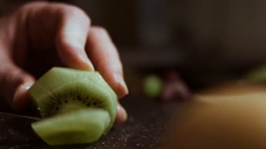 Siyah mermer kesme tahtasında sulu yeşil bir kivi dilimliyorum. Makro görünüm
