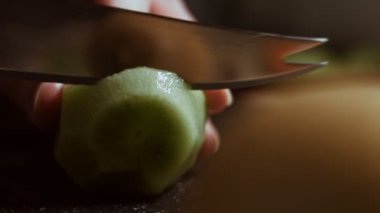 Siyah mermer kesme tahtasında sulu yeşil bir kivi dilimliyorum. Makro görünüm
