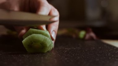 Siyah mermer kesme tahtasında sulu yeşil bir kivi dilimliyorum. Makro görünüm