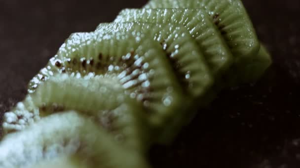 Sappige verse kiwi fruitschijfjes op een zwart marmeren snijplank. Macro uitzicht. Langzame beweging — Stockvideo