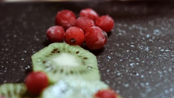 Soczyste świeże plasterki kiwi i mrożona czerwona porzeczka ułożone w kształcie choinki na czarnej marmurowej desce do krojenia. Jedzenie na święta. Zdrowa przekąska. Widok makro — Wideo stockowe