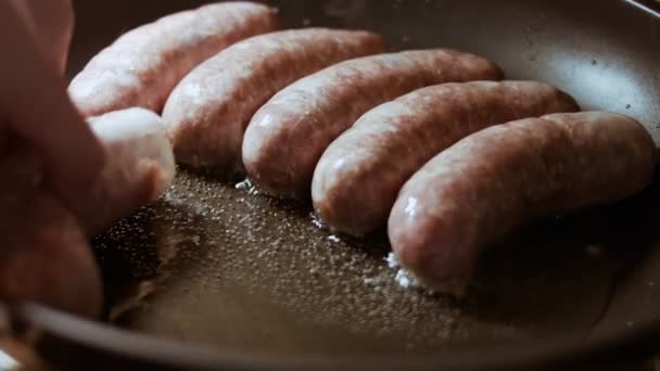 Egy közeli felvételen a szakácsok kolbászt tesznek egy fekete serpenyőbe. Kolbász főzés fekete serpenyőben olajjal. — Stock videók