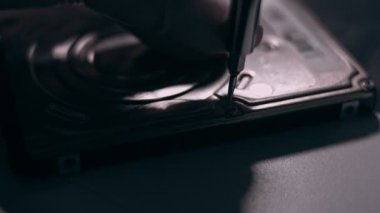 Yakın plan. Tornavida, bilgisayarın sabit diskindeki vidayı söküyor. Erkek eller bilgisayar sabit diskindeki vidayı tornavidayla büker. Bilgisayar sabit diskini onarma ustasının elleri HDD