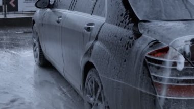 Beyaz köpükle kaplı ve su tabancasından sıçramış lüks araba yıkama işlemi. Köpük, parlak arabanın dış tarafında ağır çekimde yayılıyor..