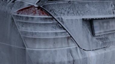 Beyaz köpükle kaplı ve su tabancasından sıçramış lüks araba yıkama işlemi. Parlak araba dış yüzeyine köpük saçılıyor. Güzel bir ortam. 4K video