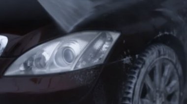 Araba yıkama servisi. Köpüğü yüksek basınçlı suyla durulamak ve yıkamak. Kiraz rengi lüks araba. Güzel bir ortam. 4K video