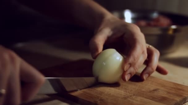 Primer plano de las manos femeninas cortando la mitad de la cebolla en cubos con un cuchillo en la tabla de madera. Proceso de preparación de ravioles en casa. 4 K video — Vídeos de Stock