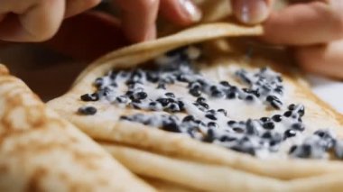 Krep üzerine taramasalata katılmış siyah balık yumurtası yaymak. Blini 'yi yuvarlıyorum. İzole edilmiş yakın çekim makro. 4K video