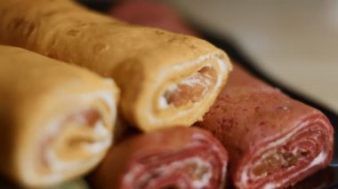 İnce, renkli krepler. Kırmızı, sarı ve yeşil kesimli krem peynirli ve somon balıklı krep. 4K video. Yavaş çekim