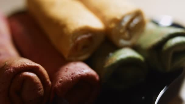 Tenké chutné barevné palačinky. Makro pohled na červené, žluté a zelené rolované palačinky se smetanovým sýrem a lososovou náplní na misce. Video 4K. — Stock video