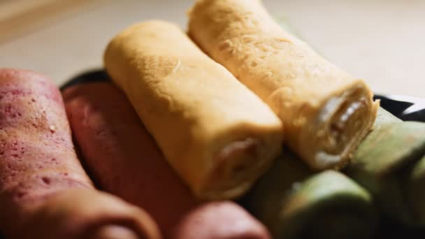 Λεπτές νόστιμες πολύχρωμες τηγανίτες. Γκρο πλαν άποψη του κόκκινου, κίτρινο και πράσινο έλασης τηγανίτες με τυρί κρέμα και γέμιση σολομού σε ένα πιάτο. Βίντεο 4K. Επιβράδυνση — Αρχείο Βίντεο