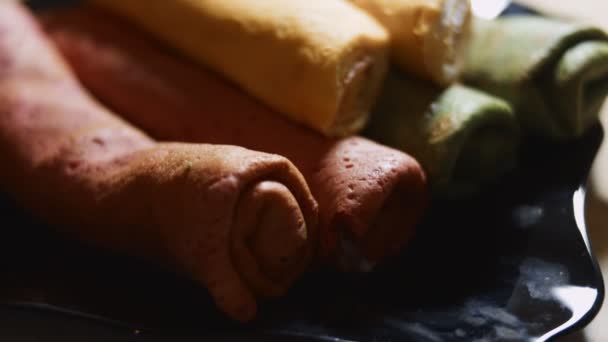 Panquecas coloridas saborosas finas. Vista macro de panquecas vermelhas, amarelas e verdes com creme de queijo e recheio de salmão em um prato. Vídeo 4K. Movimento lento — Vídeo de Stock