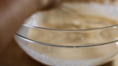 Taze yumurta, un ve sütü cam bir kasede çelik elle karıştırmanın makro görüntüsü. Krep hazırlama süreci. 4K video