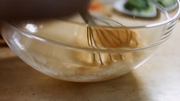Смешивание свежих яиц со стальным миксером в стеклянной чаше. Процесс приготовления блинчиков. 4K видео — стоковое видео