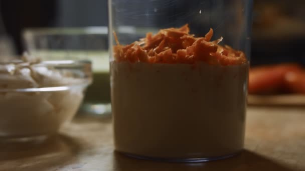 Προσθέτουμε το τριμμένο καρότο σε ένα ποτήρι πριν ανακατέψουμε τα υλικά με ένα μπλέντερ χειρός. Διαδικασία παρασκευής πολύχρωμων τηγανίτες. Βίντεο 4K — Αρχείο Βίντεο